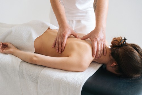 Male masseur massaging back and shoulder blades of young woman lying on massage table on white background. Concept of massage spa treatments.