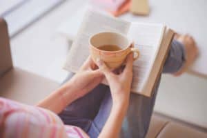 close-up-of-female-hands-holding-teacup-in-front-of-opened-book
