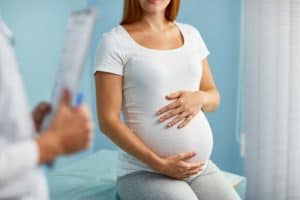 pregnant-woman-with-hands-on-stomach-talking-to-obstetrician